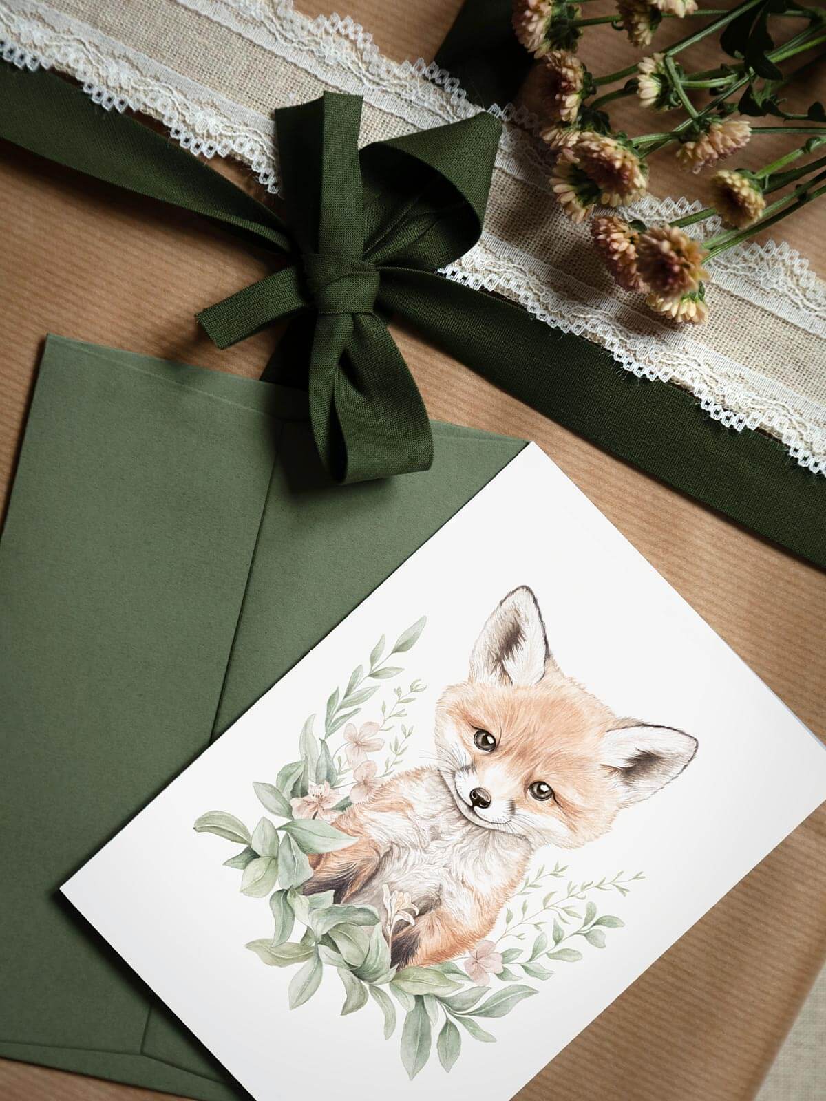 Närbild av akvarellkort A6 med räven Remi och grönt kuvert på presentpaket med blomma
