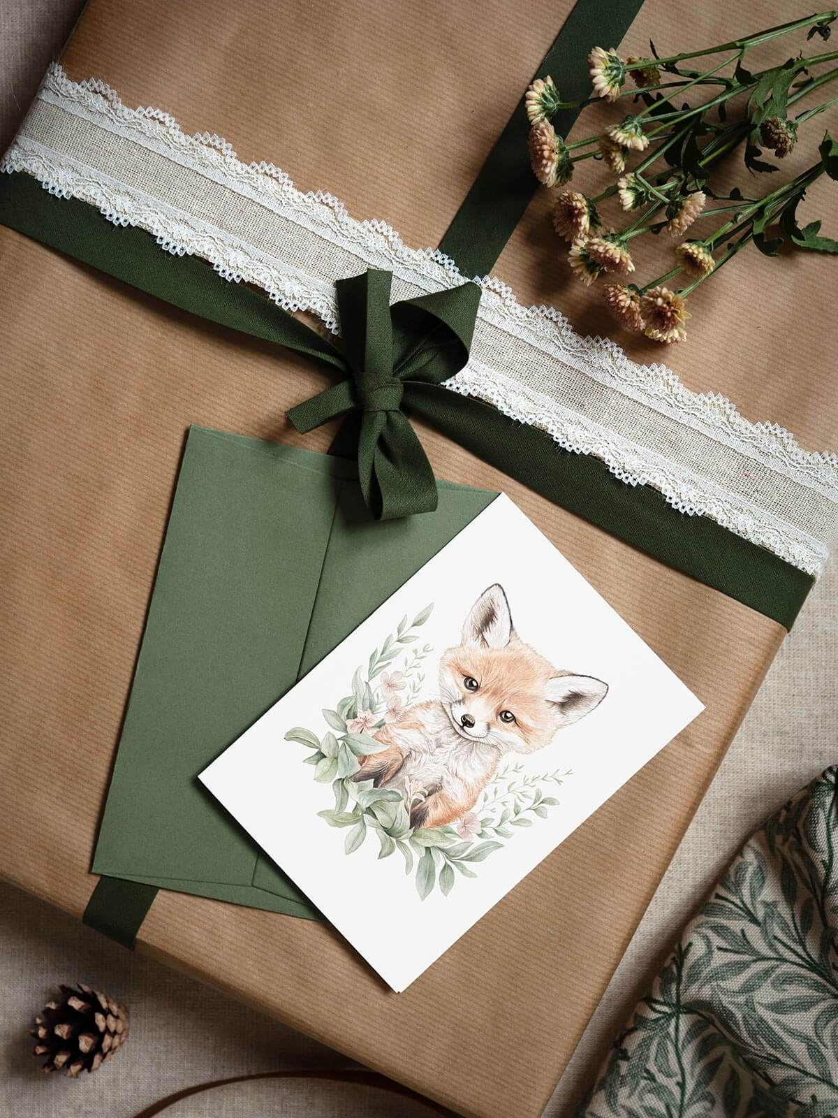 Akvarellkort A6 med räven Remi och grönt kuvert omgivet av presentpaket, blomma och kottar