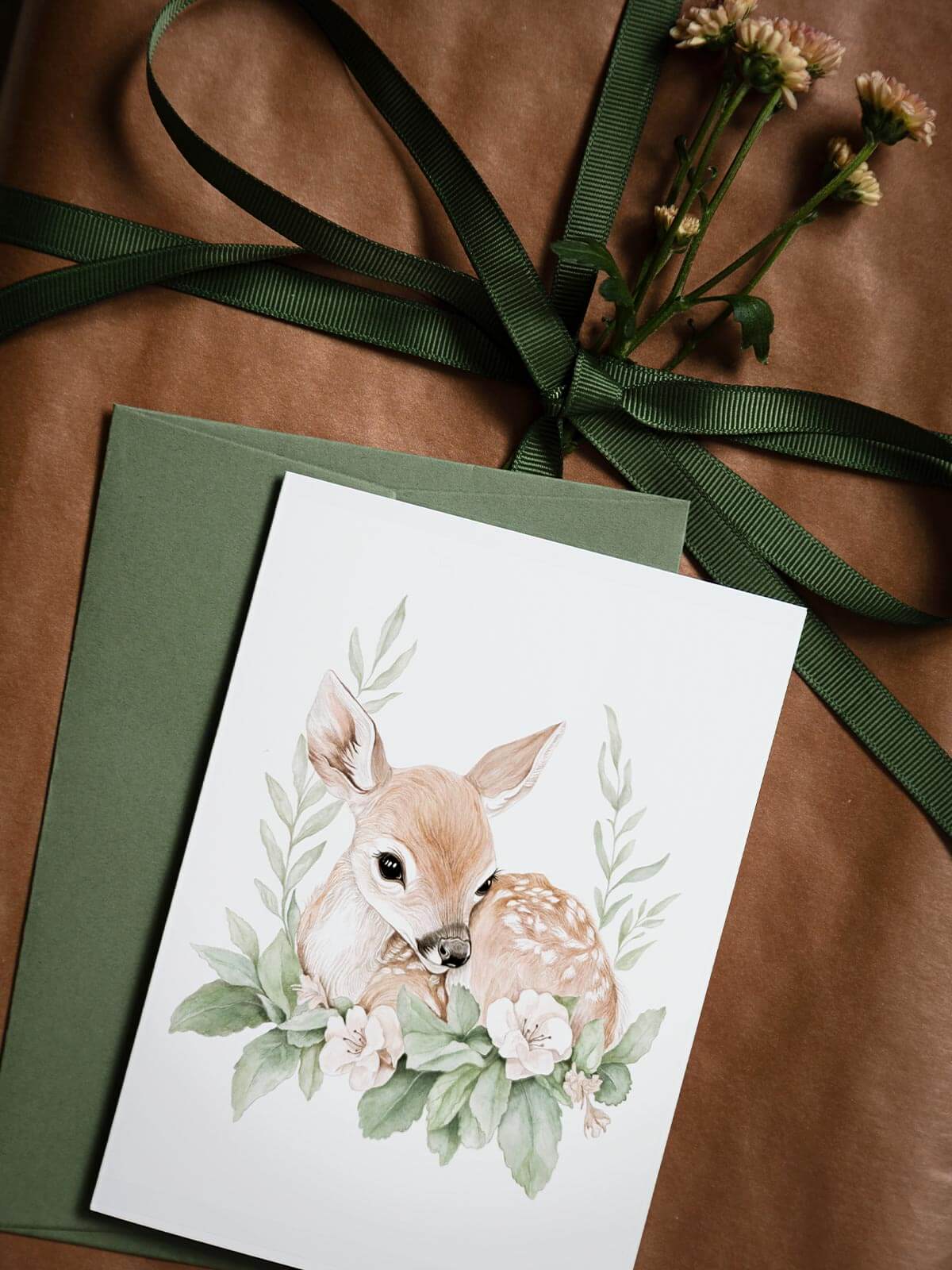 Närbild av akvarellkort A6 med rådjuret Luna och grönt kuvert på presentpaket med blomma