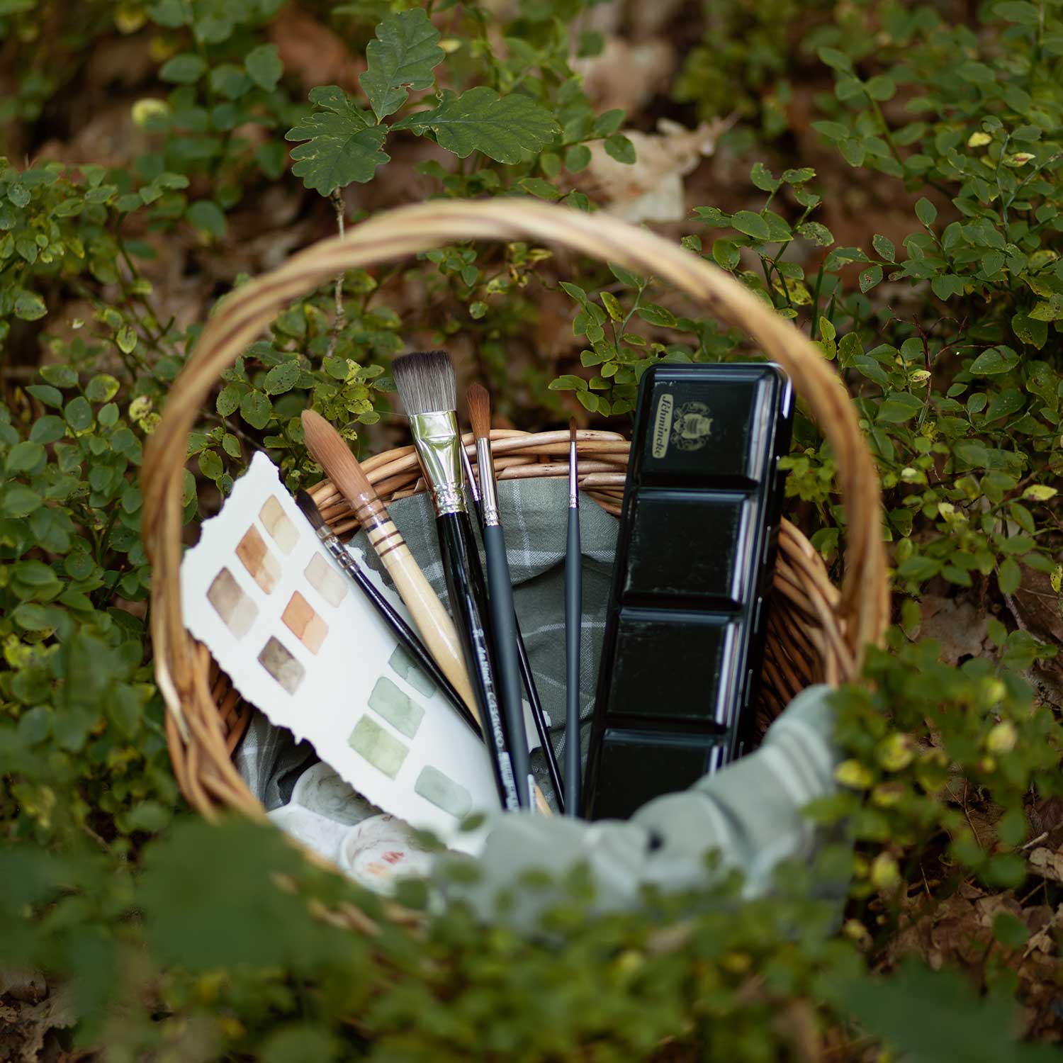 Watercolor brushes and paints among blueberry bushes in the forest
